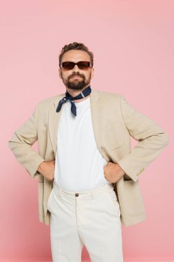 stylish french man in neck scarf and sunglasses holding posing with hands on hips isolated on pink  clipart