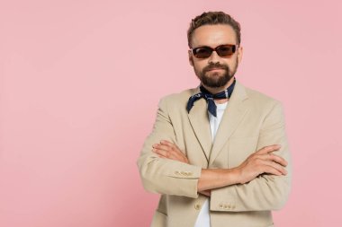 Boyunluk ve güneş gözlüklü şık Fransız adam pembe kolları çapraz duruyor. 