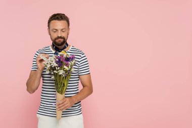 Çizgili tişört ve boyun atkısı giyen sakallı Fransız adam pembe üzerinde yaban çiçekleri tutuyor.  