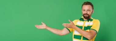 Çizgili eşarplı ve sarı tişörtlü sakallı futbol fanatiği kameraya bakarken yeşil pankartta izole edilmiş elleri gösteriyor. 