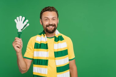 Çizgili eşarplı neşeli futbol fanatiği yeşil üzerine izole edilmiş plastik el çırpıcısı tutuyor. 