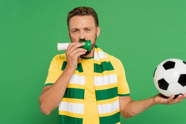 bearded sports fan holding football and blowing horn while cheering isolated on green  clipart
