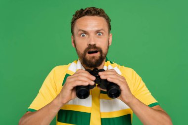 shocked man in striped scarf holding binoculars during football match isolated on green clipart