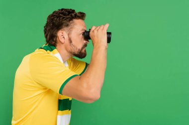 side view of bearded man in striped scarf holding binoculars during football match isolated on green clipart