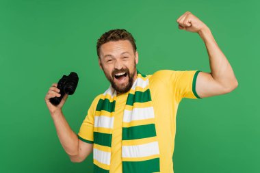 Futbol maçında elinde dürbün tutan çizgili eşarplı heyecanlı adam yeşilde izole edilmiş.