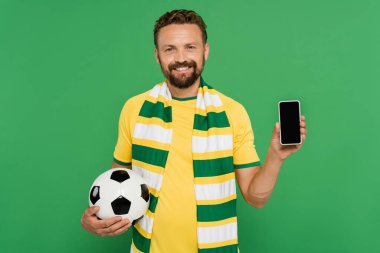 Çizgili eşarplı neşeli adam elinde futbol topu ve yeşil ekranlı akıllı telefon tutuyordu.