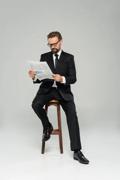 Empresário Terno Óculos Leitura Jornal Enquanto Sentado Cadeira Alta Isolado — Fotografia de Stock