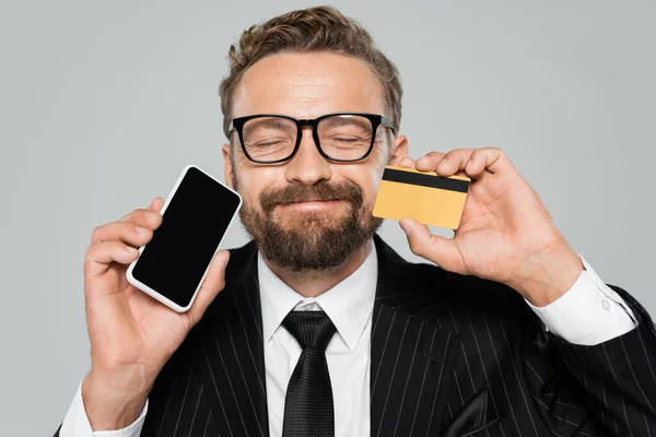 スーツを着た幸せなビジネスマンとグレーで隔離されたスマートフォンやクレジットカードを持っている — ストック写真