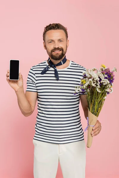 身穿条纹T恤和领巾的快乐男人 手持野花和智能手机 屏幕空白 粉色孤立 — 图库照片