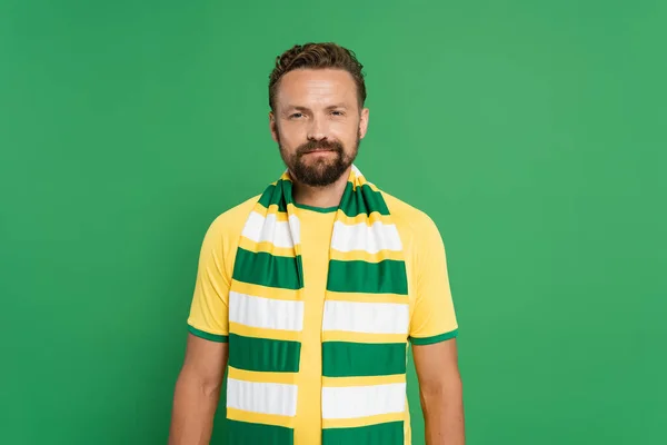 stock image bearded sports fan in striped scarf and yellow t-shirt looking at camera isolated on green 