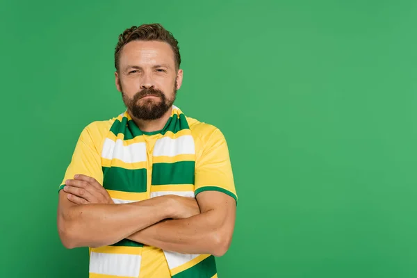 stock image offended soccer fan in striped scarf and yellow t-shirt standing with folded arms isolated on green 