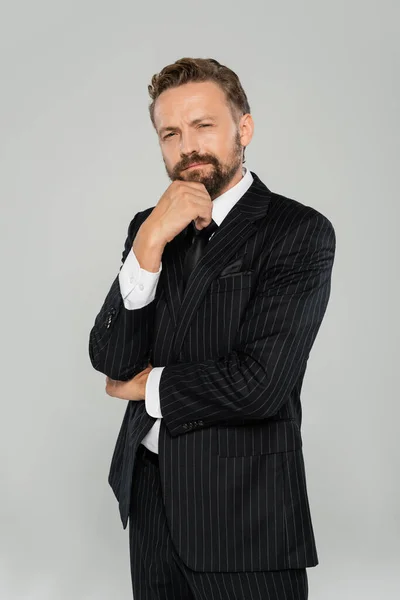 stock image pensive and bearded man in formal wear looking at camera isolated on grey 