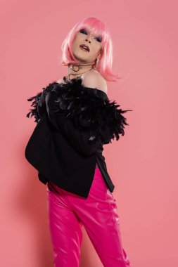 Pembe arka planda poz verirken peruk ve ceket giymiş iyi giyimli travesti bakışları. 