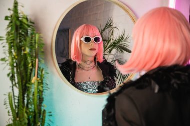 Evde aynanın yanında duran peruklu ve güneş gözlüklü moda travesti. 
