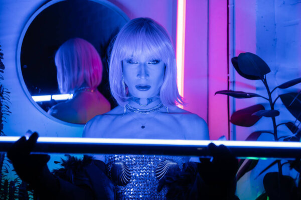Стильный трансвестит в парике с размытой флуоресцентной лампой дома