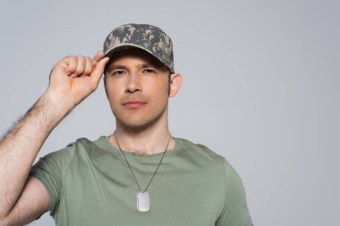 Tişörtlü Amerikalı asker, anma gününde askeri şapkasını düzeltiyor. Gri yolda izole edilmiş.