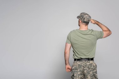 Askeri üniformalı asker ve gri arka planda selam duruşu. 
