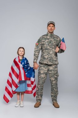 Amerikan bayrağı taşıyan askeri üniformalı bir asker ve gri üzerine mutlu bir kızın eli. 