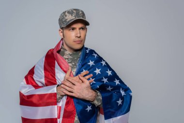 Amerika Birleşik Devletleri bayrağına sarılı, kamuflaj üniforması içindeki vatansever asker, gri üzerinde izole edilmiş bir anma gününde. 
