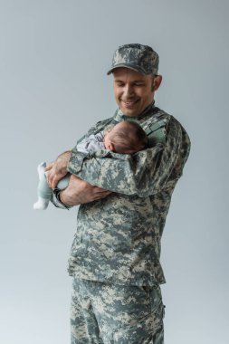 Üniformalı ve şapkalı neşeli asker. Yeni doğan oğlu gri yolda izole edilmiş. 