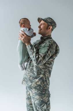 happy military soldier in uniform holding newborn son in arms isolated on grey  clipart