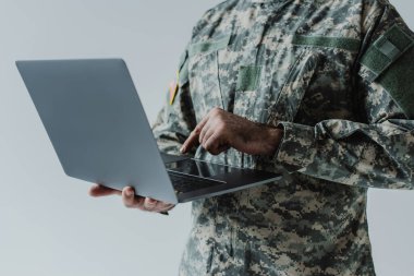 Asker üniformalı askerin gri üzerine izole edilmiş dizüstü bilgisayar kullanışının görüntüsü. 