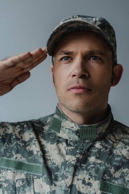 sad soldier in military uniform crying and saluting during memorial day isolated on grey 