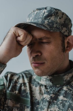 Askeri üniformalı üzgün asker. Gri üzerinde izole edilmiş bir anma gününde gözleri kapalı ağlıyor. 