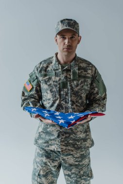 Üniformalı Amerikan askeri, gri üzerine izole edilmiş anma günü boyunca ABD bayrağını elinde tutuyordu. 