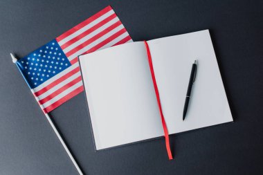Siyah üzerine izole edilmiş boş defter yakınında çizgili Amerikan bayrağının üst görünümü 