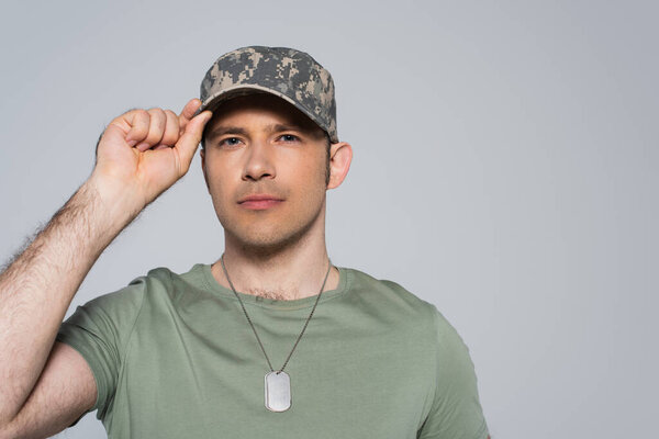 American soldier in t-shirt adjusting military cap during memorial day isolated on grey