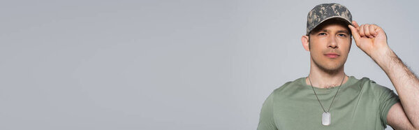 American soldier in t-shirt adjusting military cap during memorial day isolated on grey, banner 
