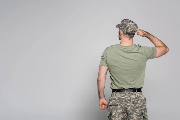Zadní Pohled Vojáka Vojenské Uniformě Čepici Salutování Šedém Pozadí — Stock fotografie
