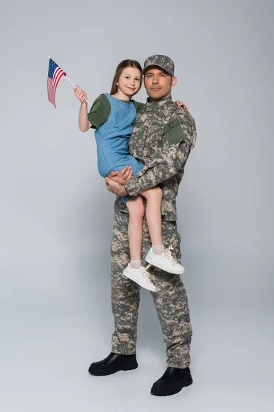 Военнослужащий Военной Форме Держащий Руках Веселую Дочь Американским Флагом Сером — стоковое фото