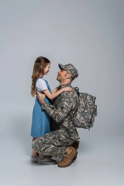 身着军服背着背包的快乐军人在灰色背景下拥抱着快乐的女儿 — 图库照片