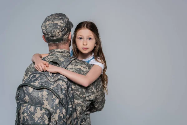 daughter hugging father in military uniform during homecoming isolated on grey