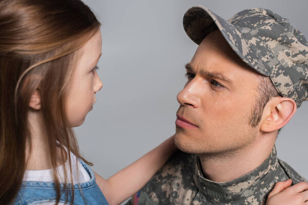 Девушка смотрит на грустного военнослужащего в военной форме плачущего во время памятного дня, изолированного на сером 