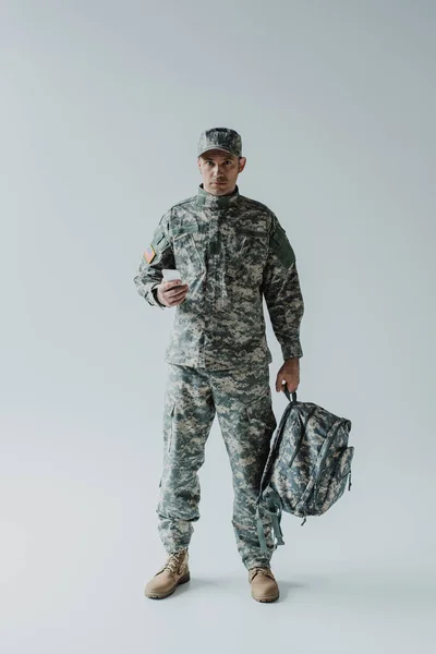 Amerikan Askeri Sırt Çantası Tutarken Akıllı Telefon Kullanıyor Gri Üzerinde — Stok fotoğraf