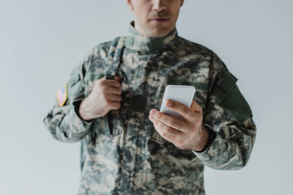 cropped view of serviceman in army uniform using mobile phone isolated on grey 