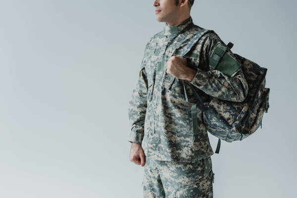 cropped view of serviceman in army uniform standing with backpack isolated on grey 