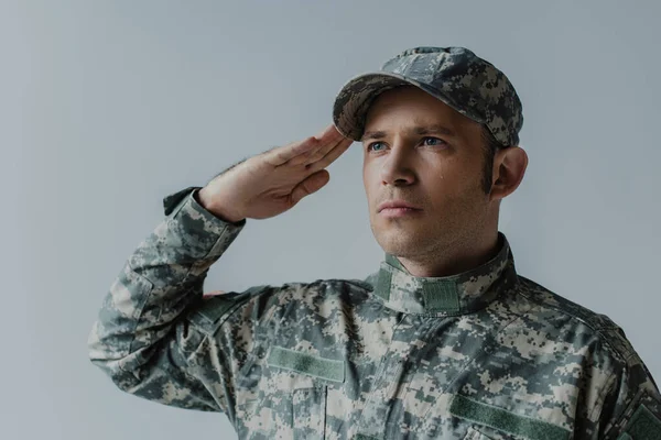 sad military man crying while saluting during memorial day isolated on grey