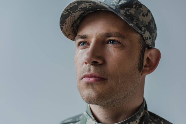 храбрый солдат в военной форме со слезой на лице, изолированной от серого 