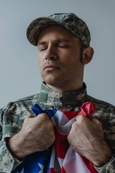 Американский солдат, держащий флаг США во время плача в день памяти, изолированный на сером 