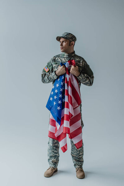 полная длина американского солдата, держащего флаг США в день памяти на сером 
