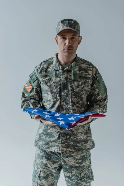 American soldier in uniform holding folded flag of United States during memorial day isolated on grey