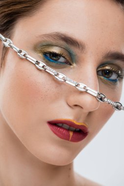 close up of young woman with shiny eye makeup and silver chain on face isolated on grey  clipart
