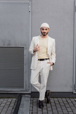 İyi giyimli eşcinsel adam poz veriyor ve binanın yakınındaki kameraya bakıyor. 