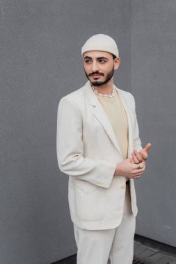 Şapkalı ve bej takım elbiseli moda eşcinsel adam binanın yanında duruyor. 