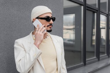 Güneş gözlüklü moda homoseksüel adam şehir caddesinde cep telefonuyla konuşuyor. 