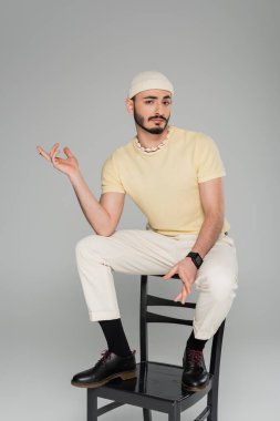 Kafası karışmış şapkalı eşcinsel adam gri sandalyede tek başına oturuyor.  
